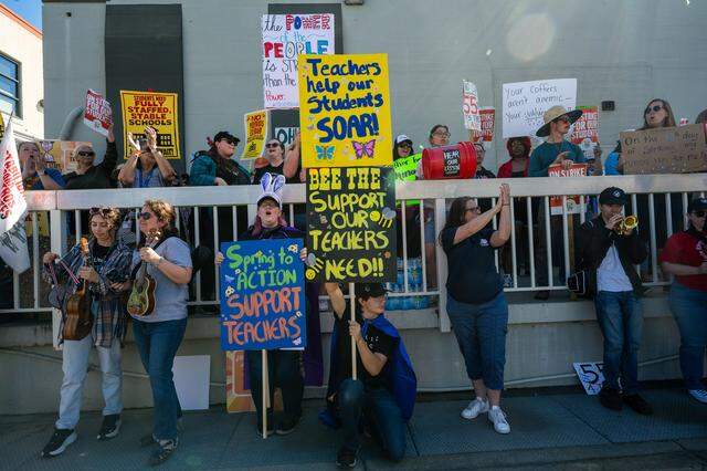 Cassie Harvey, a parent and para-educator, center left, and Amanda Rayls, center right, hold signs as they join more than a thousand teachers and parents rallying at the Twin Rivers Unified School District office Friday.