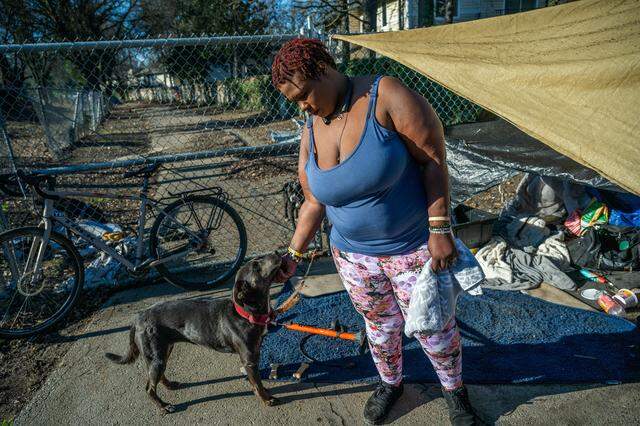 Elizabeth Williams, 38, scratches the chin of one of her three service dogs, Little Baby, near an improvised tarp shelter in South Natomas on Jan. 13. After multiple encampment sweeps, she no longer has a tent or many of her belongings, and she is suing the city in small claims court for the losses.