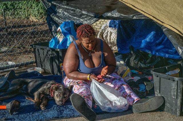 Elizabeth Williams, 38, prepares hamburgers beside one of her three service dogs, Little Baby, underneath an improvised tarp shelter in South Natomas on Jan. 13, 2026. Williams said that losing her belongings undermined the bit of stability she had. Since March 2025, she dropped out of online classes she was taking because her laptop was discarded as trash.  After her debit card was thrown away in a sweep, she couldn’t pay her phone bill, and she lost the number she had kept for years — making it more difficult for social services agencies to contact her.