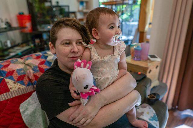Transportation Security Officer Mary Becker, 31, cuddles with her 14-month-old daughter, Alice, in their living room in Roseville on Thursday, March 26, 2026. Becker, a single mother who has worked at Sacramento International Airport since 2016, is concerned about the impact of the federal government shutdown. "We have lost 2-1/2 paychecks, and now we are looking at a third,” she said.