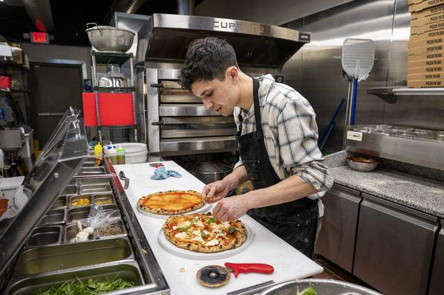 Manager Jackson Wells adds toppings to a pizza order at Dodici Pizza on March 6 in Sacramento.