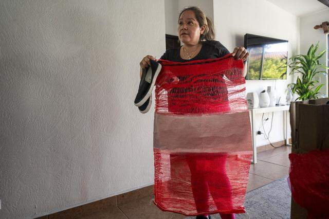 Maria de Jesus Estrada Juarez stands inside a home in Rosarito, Mexico, on Sunday, March 29, 2026, holding the red mesh bag that contained her belongings after her detention at a green card appointment in Sacramento. “They gave me this in exchange for my life,” Estrada said. She was deported within 24 hours of her arrest and later granted humanitarian parole to return to the United States under a federal court order. 