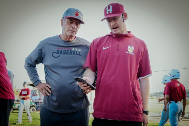 R, Head coach Griffin Teisher and Robert Bafia look over stats on a cell phone app fed from a Full Swing device on Monday, February 23, 2026 at Mission Hills H.S. in San Marcos. The device records sevral batting statistics that are a boon to player improvement and a boon to recruiters. (Sandy Huffaker / For The San Diego Union-Tribune)