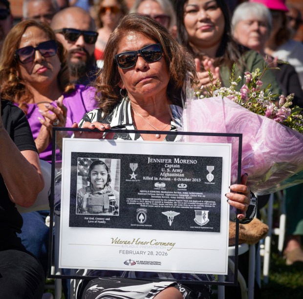 SAN DIEGO, CA - FEBRUARY 28: Maria Cordova, mother of Army nurse, Captain Jennifer Moreno, a San Diego High School graduate, killed in 2013, while supporting combat operations when providing medical assistance to wounded soldiers in Afghanistan, holds a framed poster of the plaque unveiled for her daughter, during a veteran honor ceremony and plaque presentation, at Mt. Soledad National Veterans Memorial in La Jolla, Saturday, February 28, 2026, in San Diego, California. (Howard Lipin / For The San Diego Union-Tribune)