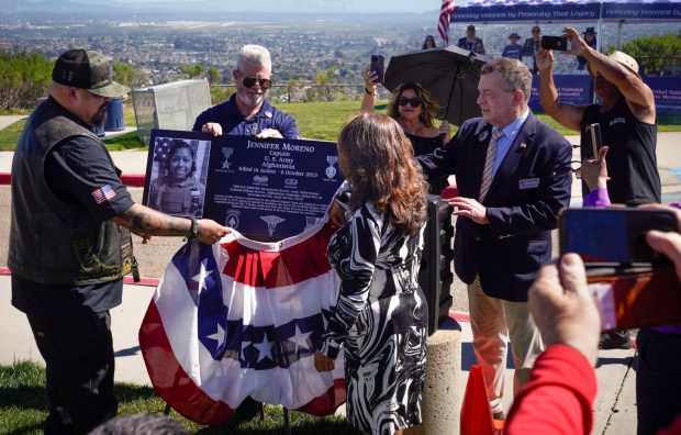 SAN DIEGO, CA - FEBRUARY 28: Assisted by Miguel Alatorre, founder of Plaques for Warriors, left, Maria Cordova, right, mother of Army nurse, Captain Jennifer Moreno, a San Diego High School graduate, killed in 2013, while supporting combat operations when providing medical assistance to wounded soldiers in Afghanistan, uncovers a photo of the plaque for her daughter, during a veteran honor ceremony and plaque presentation at Mt. Soledad National Veterans Memorial in La Jolla, Saturday, February 28, 2026, in San Diego, California. (Howard Lipin / For The San Diego Union-Tribune)