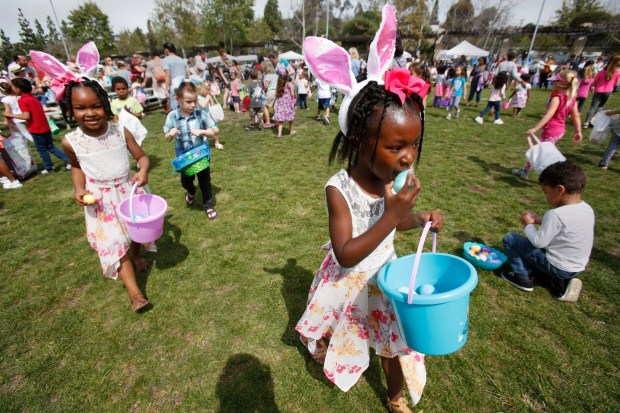 Emory Harris, 4, left, follows big sister Lyrical Harris, 5, right, as they looks for more eggs on the field at an Easter egg hunt in San Diego. (Peggy Peattie / For The San Diego Union-Tribune)