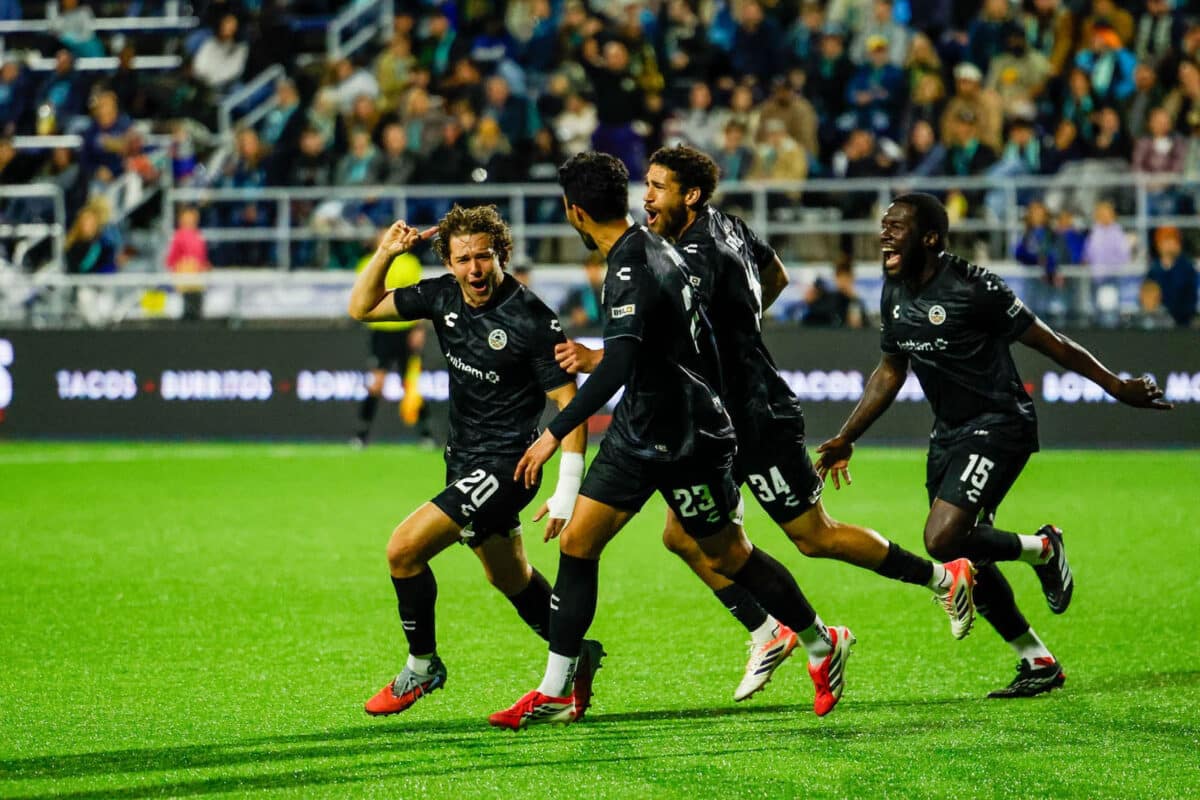 Alameda Post - Four Oakland Roots players run and celebrate in a game against Monterey Bay FC.