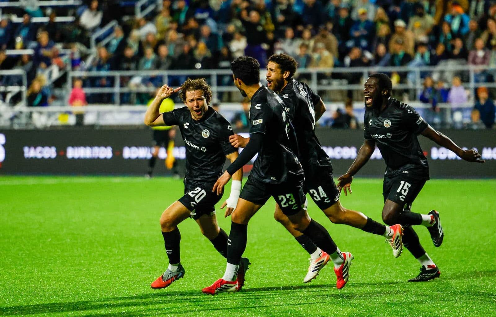 Alameda Post - Four Oakland Roots players run and celebrate in a game against Monterey Bay FC.