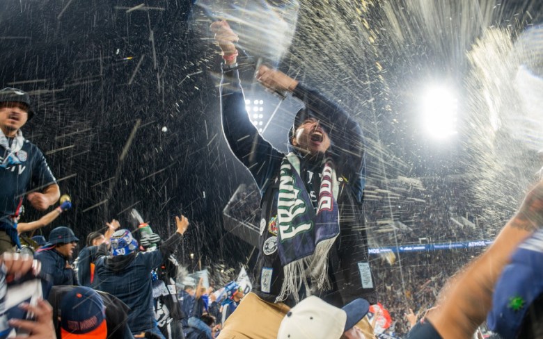 Person spraying beer in celebration at a crowded, brightly lit event.