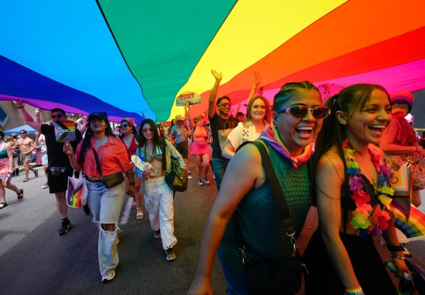 Participants take part in carrying the large Pride flag, while others enjoy walking under the flag as they march down Sixth Avenue during the San Diego Pride Parade in Hillcrest on Saturday, July 19, 2025.  (Nelvin C. Cepeda / The San Diego Union-Tribune)