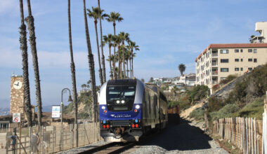 Passenger train on single track next to palm trees and beach