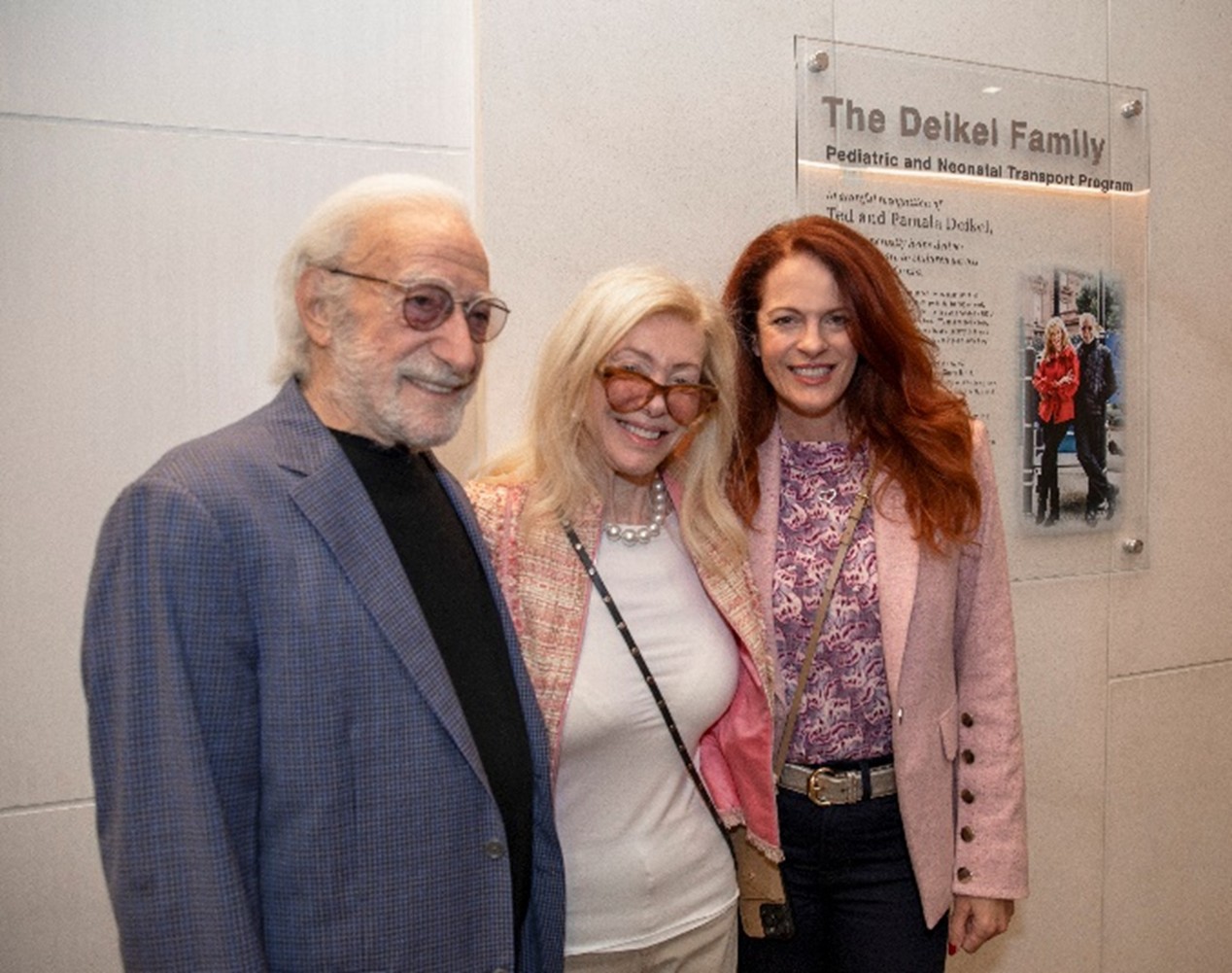 Three people stand next to one another in front of a plaque