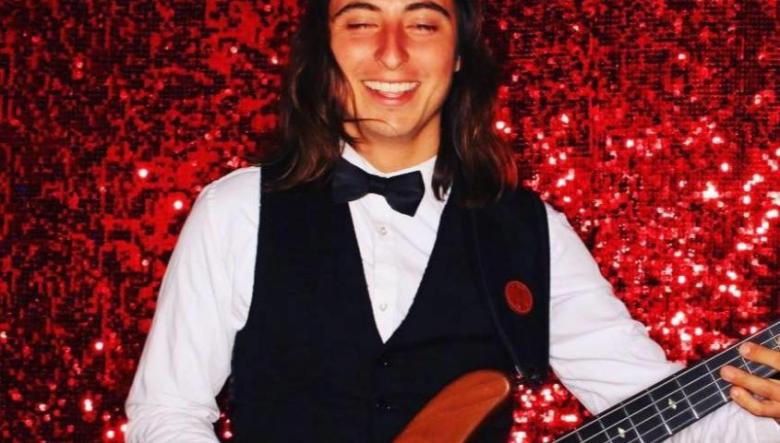 Photo of a smiling man playing a guitar against a sparkly red background