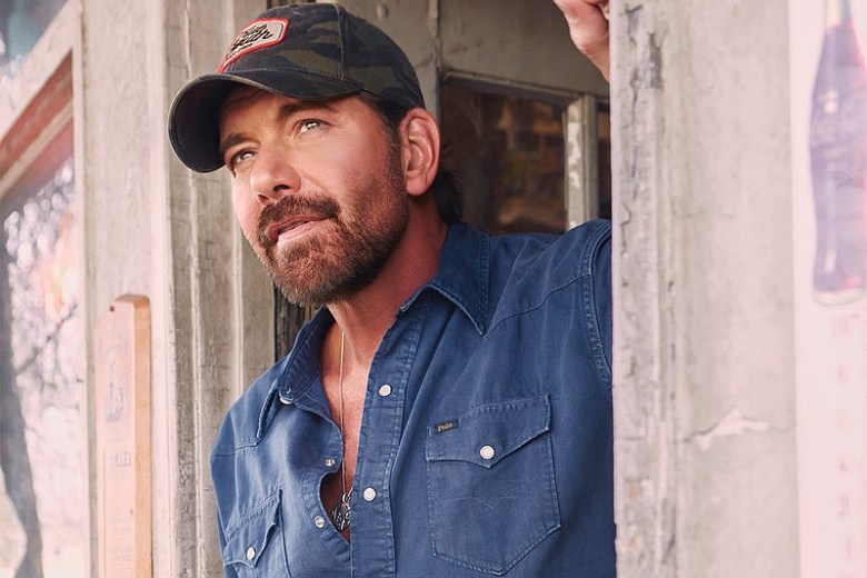 Man in a baseball cap and denim shirt posing in a doorway