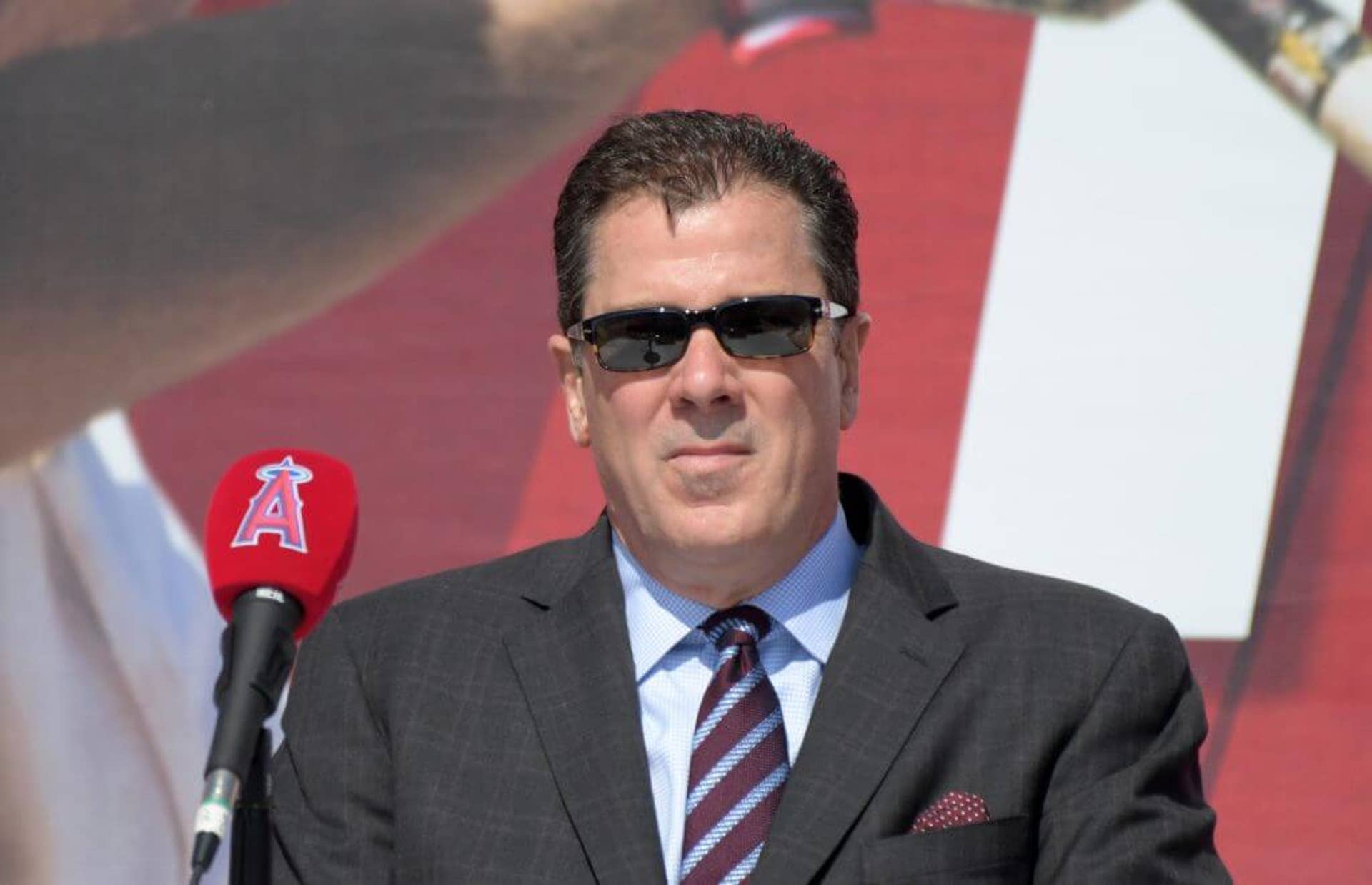 Los Angeles Angels president John Carpino, in sunglasses, stands behind an Angels-branded microphone at a press conference