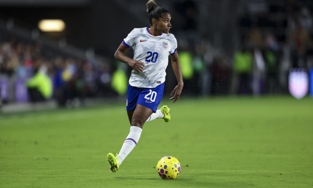 A player in a blue and white uniform dribbles a soccer ball on the field