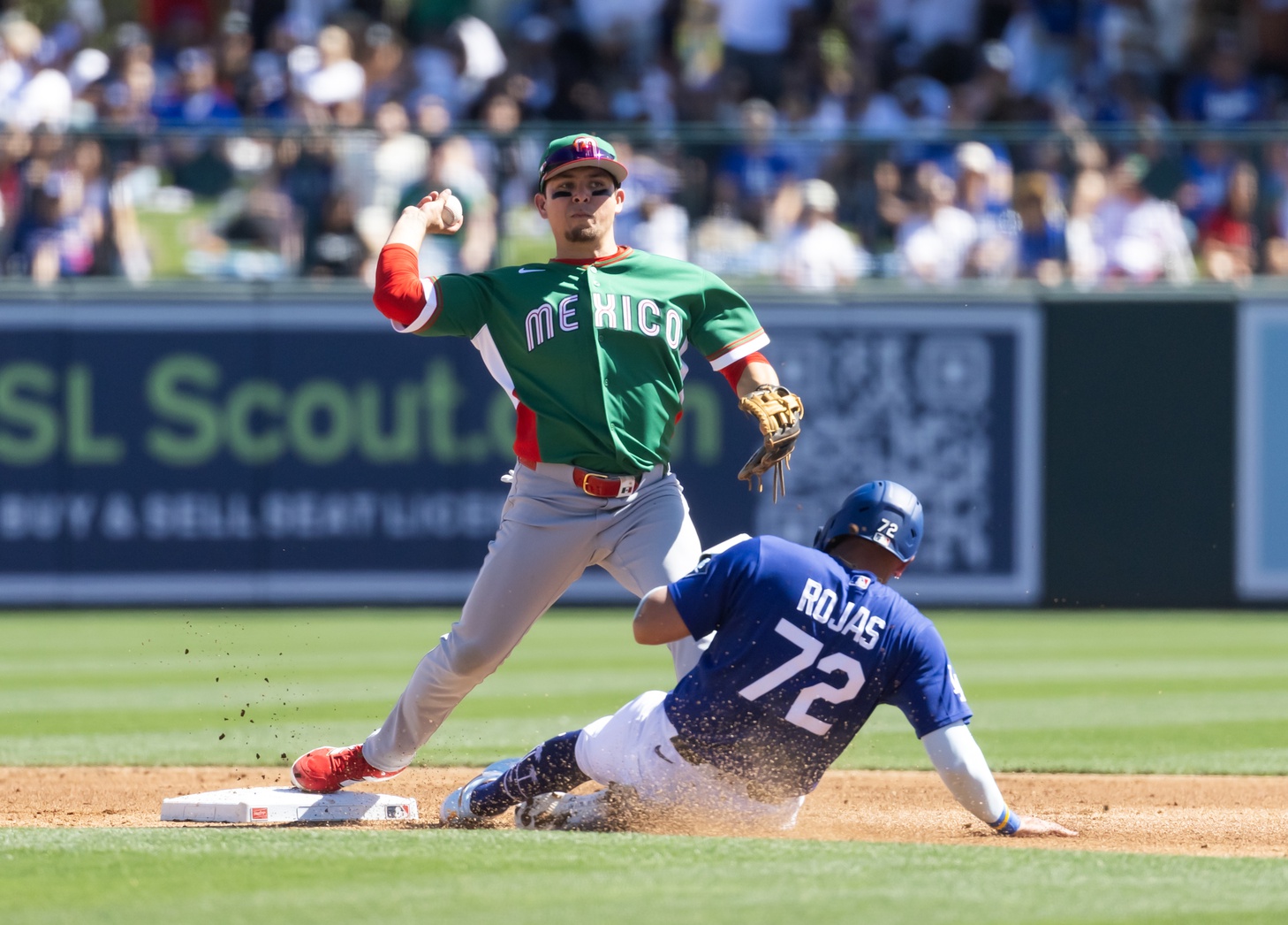 Mar 4, 2026; Glendale, AZ, USA; Team Mexico second baseman Luis Urias throws to first base after forcing out sliding Los Angeles Dodgers base runner Miguel Rojas during a spring training game at Camelback Ranch. Mandatory Credit: Mark J. Rebilas-Imagn Images