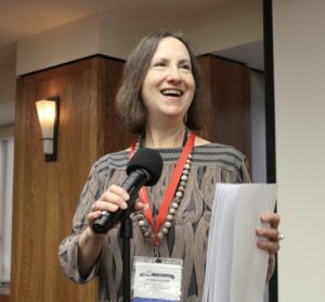 Jessica Vapnek smiles while holding a microphone during an academic conference.