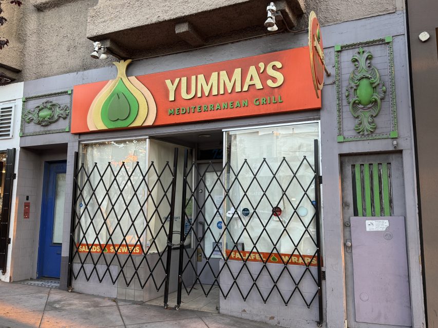 Storefront of Yumma's Mediterranean Grill with closed security gates, a red and orange sign, and decorative green accents on the exterior.