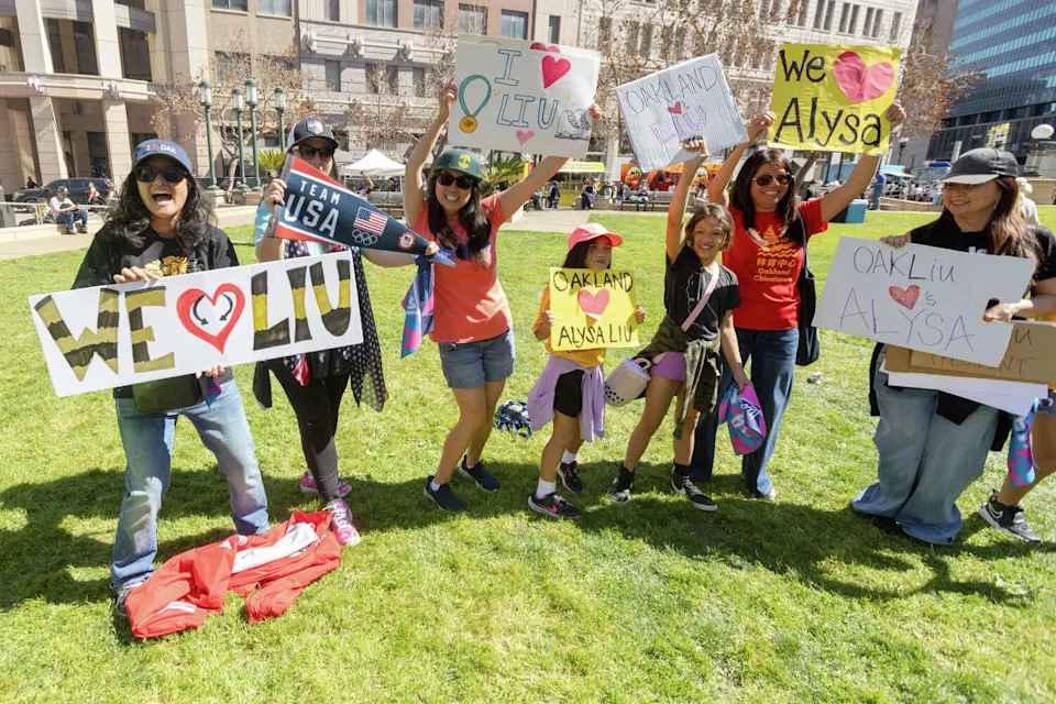 A group of Alysa Liu fans, including Aimee Eng (third from right), hold signs during the Alysa Liu Celebration Rally at Frank Ogawa Plaza in front of Oakland City Hall in Oakland, Calif., on March 12, 2026. (Douglas Zimmerman/SFGATE)