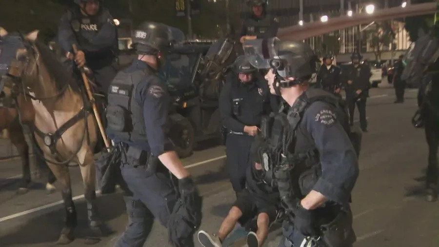Officers detain protesters as mounted police and tactical units respond to clashes during the “No Kings” protest in downtown Los Angeles.