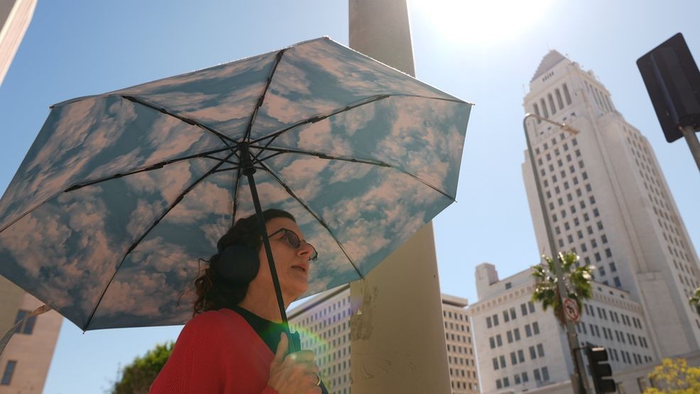 A pedestrian holds a cloud themed umbrella under a sunny day next to Los Angeles City Hall in Los Angeles Thursday, March. 12, 2026. (AP Photo/Damian Dovarganes)