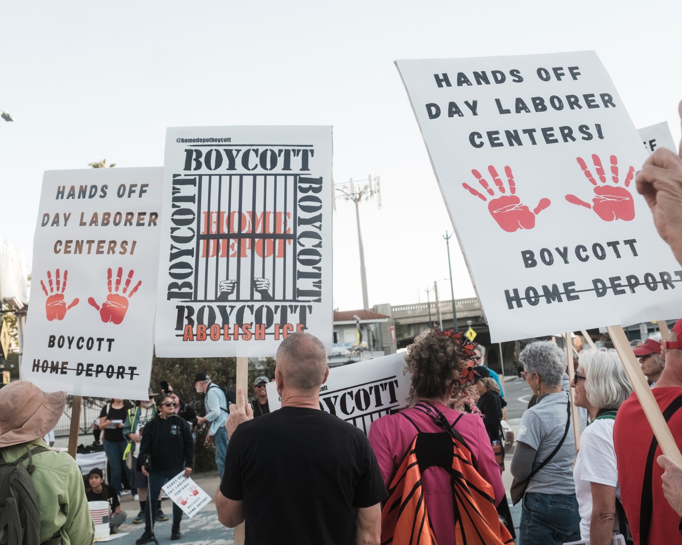 Photo of a crowd of protestors holding signs that read "Hands Off Day Laborer Centers!" and "Boycott Home Deport"