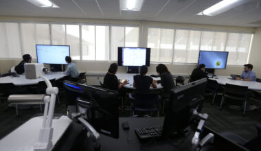 Students collaborate in a modern computer lab at Cal State LA, working at curved desks with large digital screens along a windowed wall.