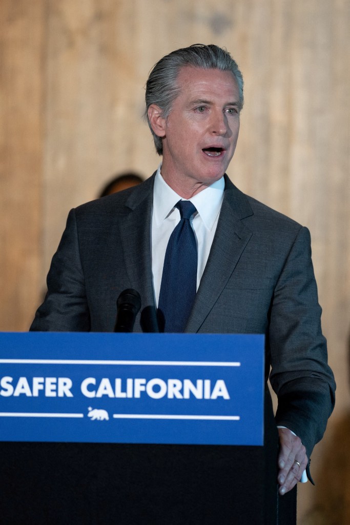 California Governor Gavin Newsom speaking at a podium with "SAFER CALIFORNIA" visible.