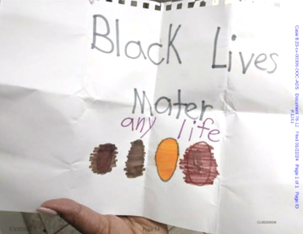 Child's drawing on white paper that says "Black Lives Mater any life" with four colored ovals underneath, held by a hand.
