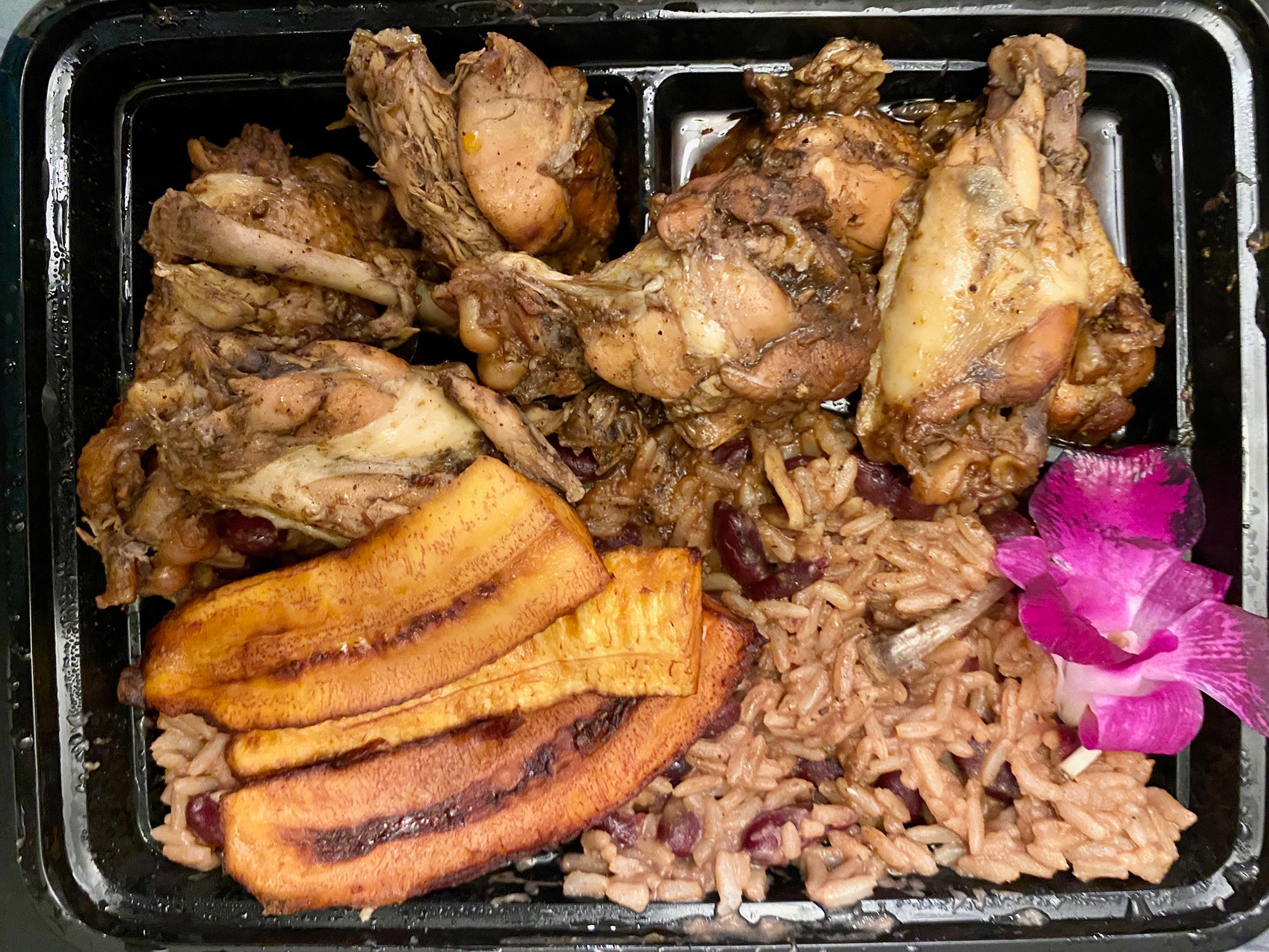 Jerk chicken, plantains and rice in a takeout container.