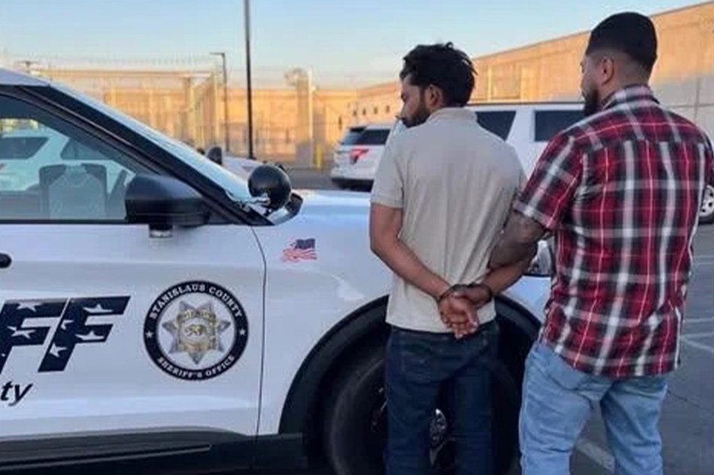 A man in handcuffs being escorted by another man next to a Stanislaus County Sheriff's Office vehicle.