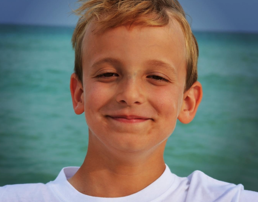 Connor Metz's legacy includes life-saving training of 1500 nursing students. Connor is pictured here smiling in front of the ocean in a white tee-shirt. He lost his life at 13 due to undiagnosed Loeys-Dietz syndrome and aortic dissection.