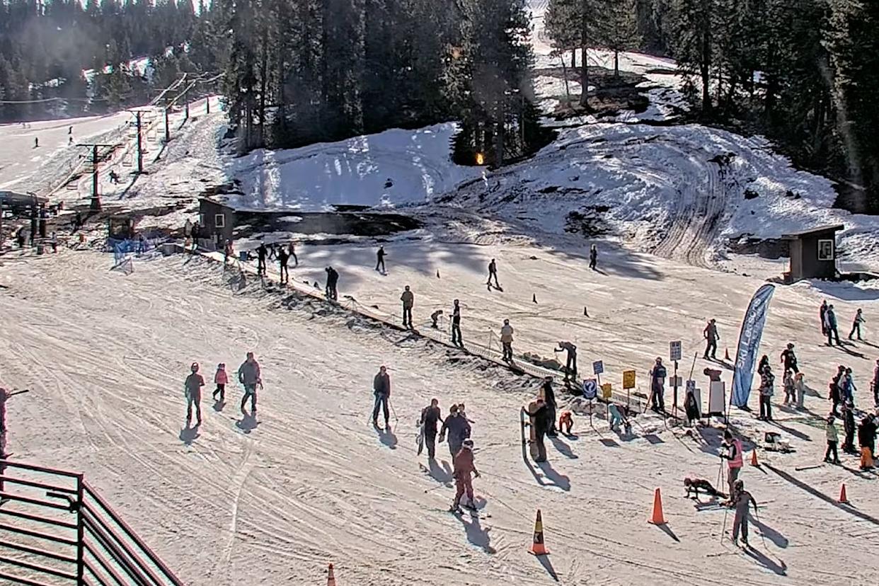A busy ski resort with people skiing and snowboarding on a sunny day.