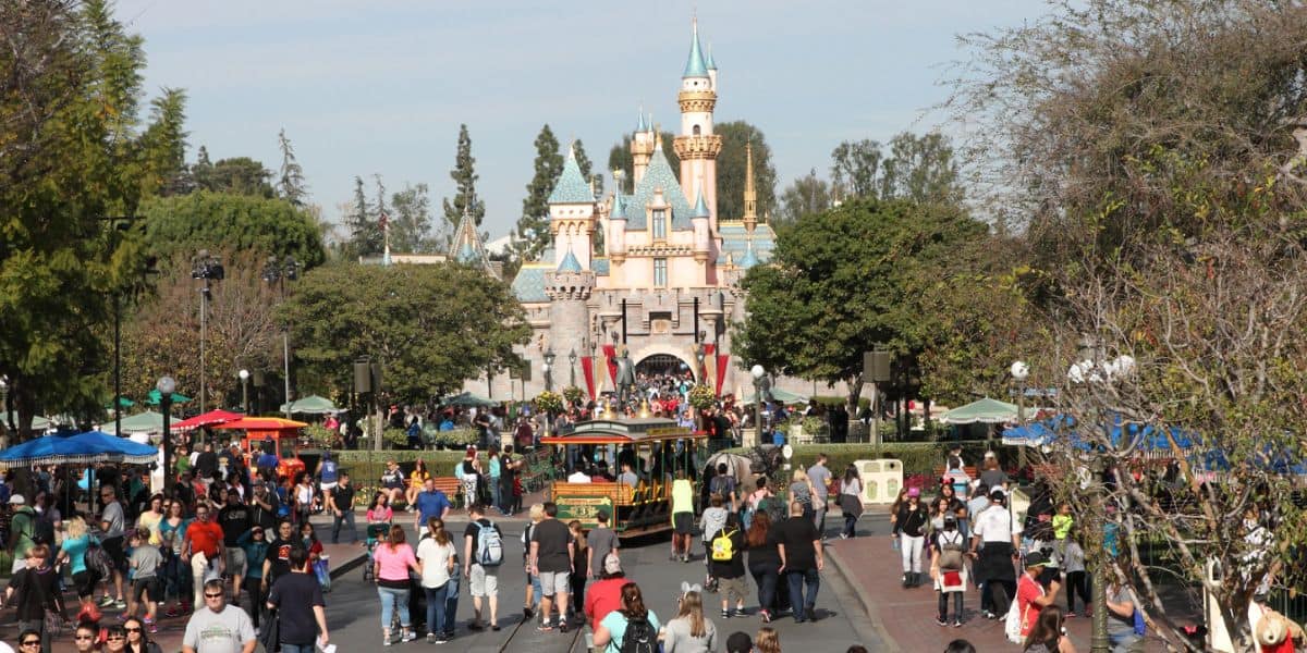 Crowds of people walk down Main Street, U.S.A., toward Sleeping Beauty Castle at Disneyland Park.
