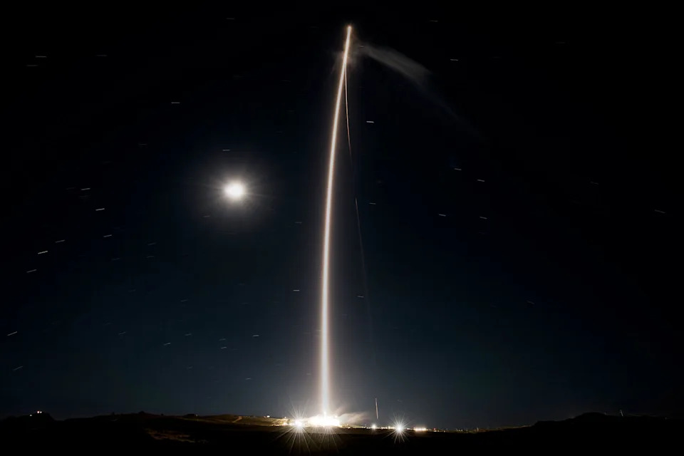 a time lapse photo captures the glowing streak of a rocket's plume as it climbs spaceward adding to the light from the moon