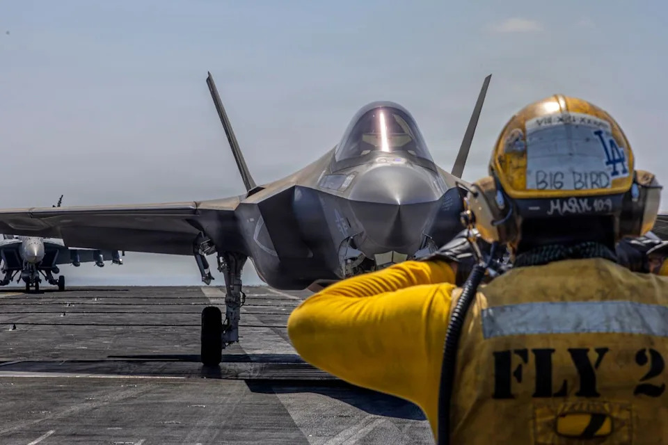 A crewman on an aircraft carrier wears a Los Angeles Dodgers sticker on his yellow helmet.