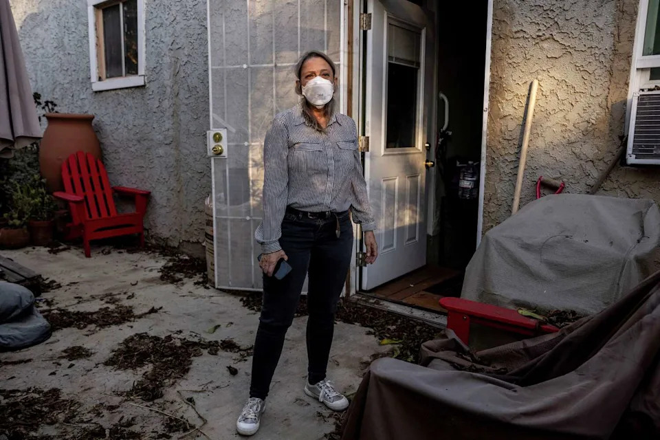 A woman stands outside her home in Altadena in October 2025. The home was damaged by smoke and soot from the Eaton Fire. (Stephen Lam/S.F. Chronicle)