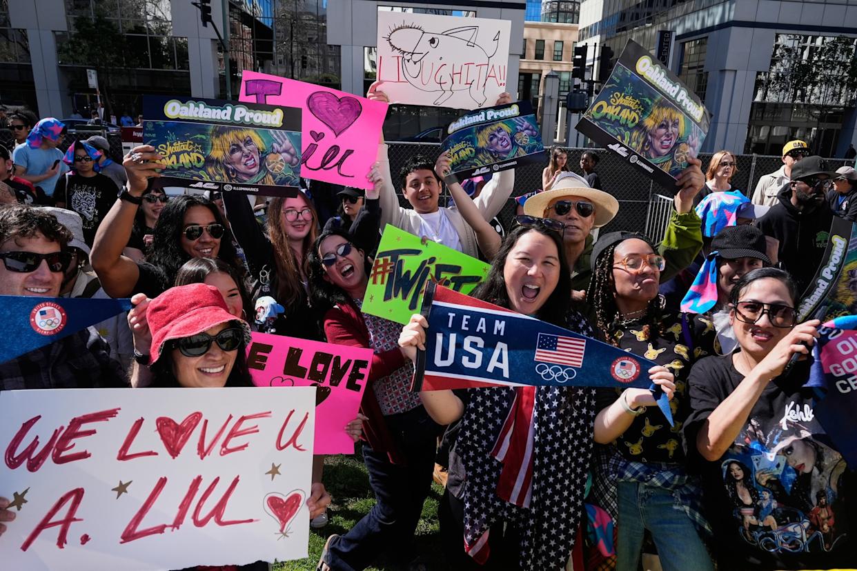 Godofredo A. Vasquez/AP - PHOTO: People hold up signs as they pose for cameras before a celebration rally for U.S. Olympic gold medalist Alysa Liu, outside City Hall, in Oakland, Calif., on March 12, 2026.