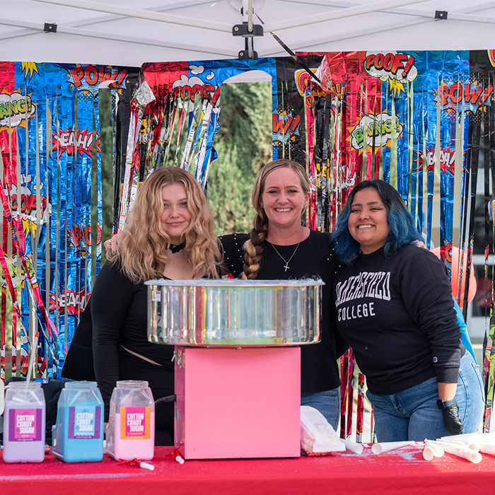 three females standing together in front of a cotton candy machine
