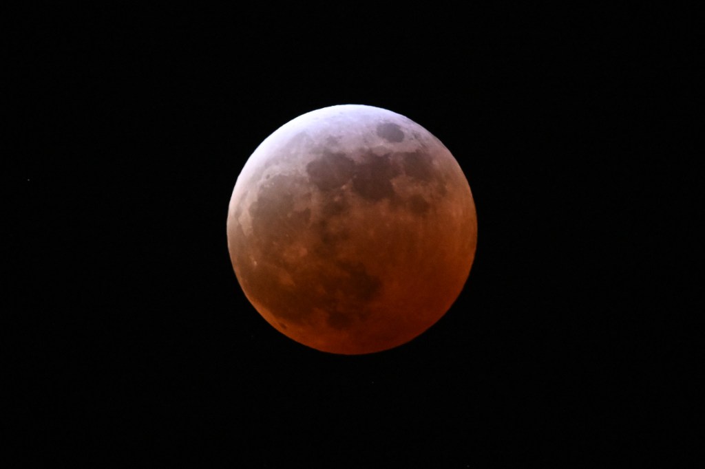 Full lunar eclipse in progress, showing the "Blood Moon" effect with the moon appearing reddish-orange against a dark sky.
