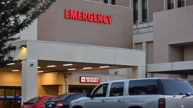 Hospital emergency entrance with large "EMERGENCY" sign and parked vehicles.
