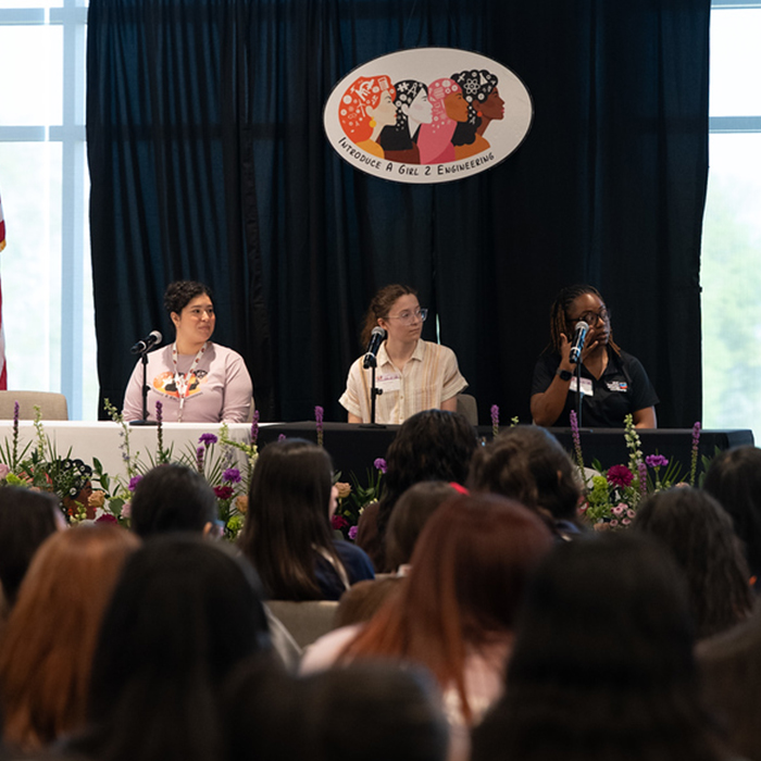 three panelists sitting at a table on stage listening to a question