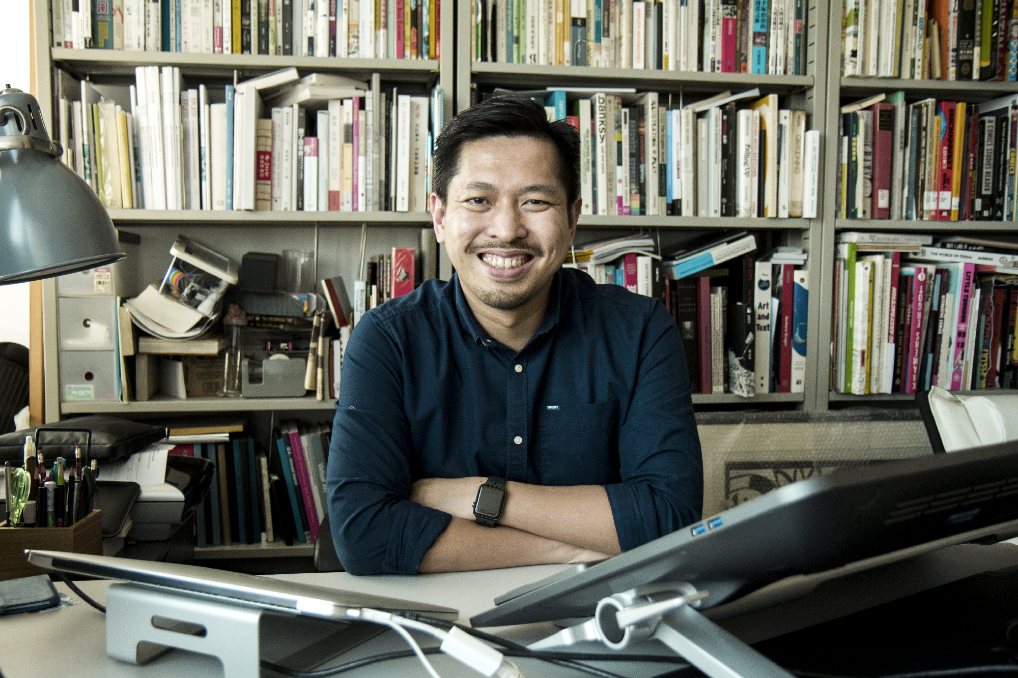 man at desk smiles in front of full bookshelves