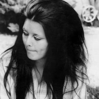 a woman with long dark hair seated outdoors in a casual pose