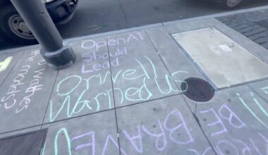 Chalk writing on a sidewalk reads, "OpenAI Should Lead Orwell Warned Us," with additional partially visible words and passing cars nearby.