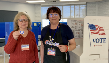 Smiling female bilingual poll workers holding up their badges.