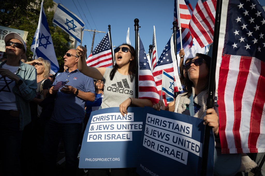 People at a "United for Israel" rally holding Israeli and American flags and signs that read "CHRISTIANS & JEWS UNITED FOR ISRAEL".