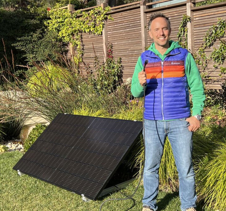 man standing next to a large solar panel holding a cord