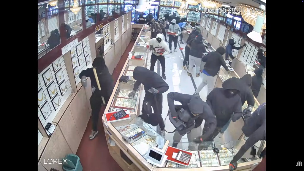Multiple masked people smash glass display cases in a jewelry store during a robbery.